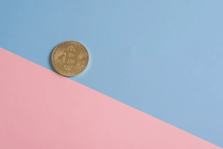 Uma moeda de bitcoin sobre um fundo dividido na diagonal entre rosa e azul.