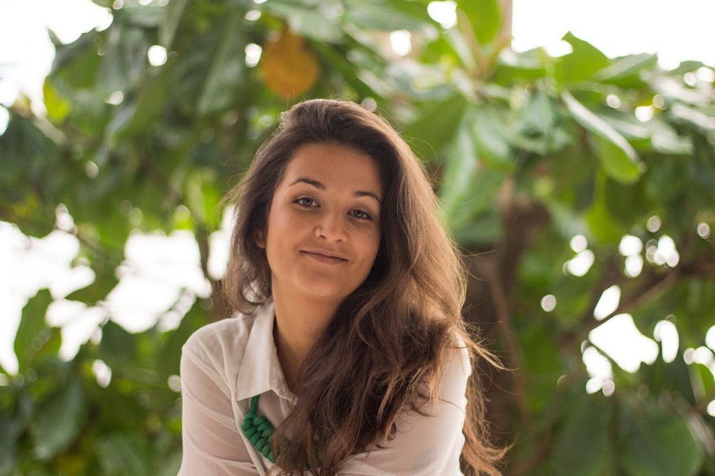 Retrato de uma mulher sorrindo sob a folhagem de uma árvore.