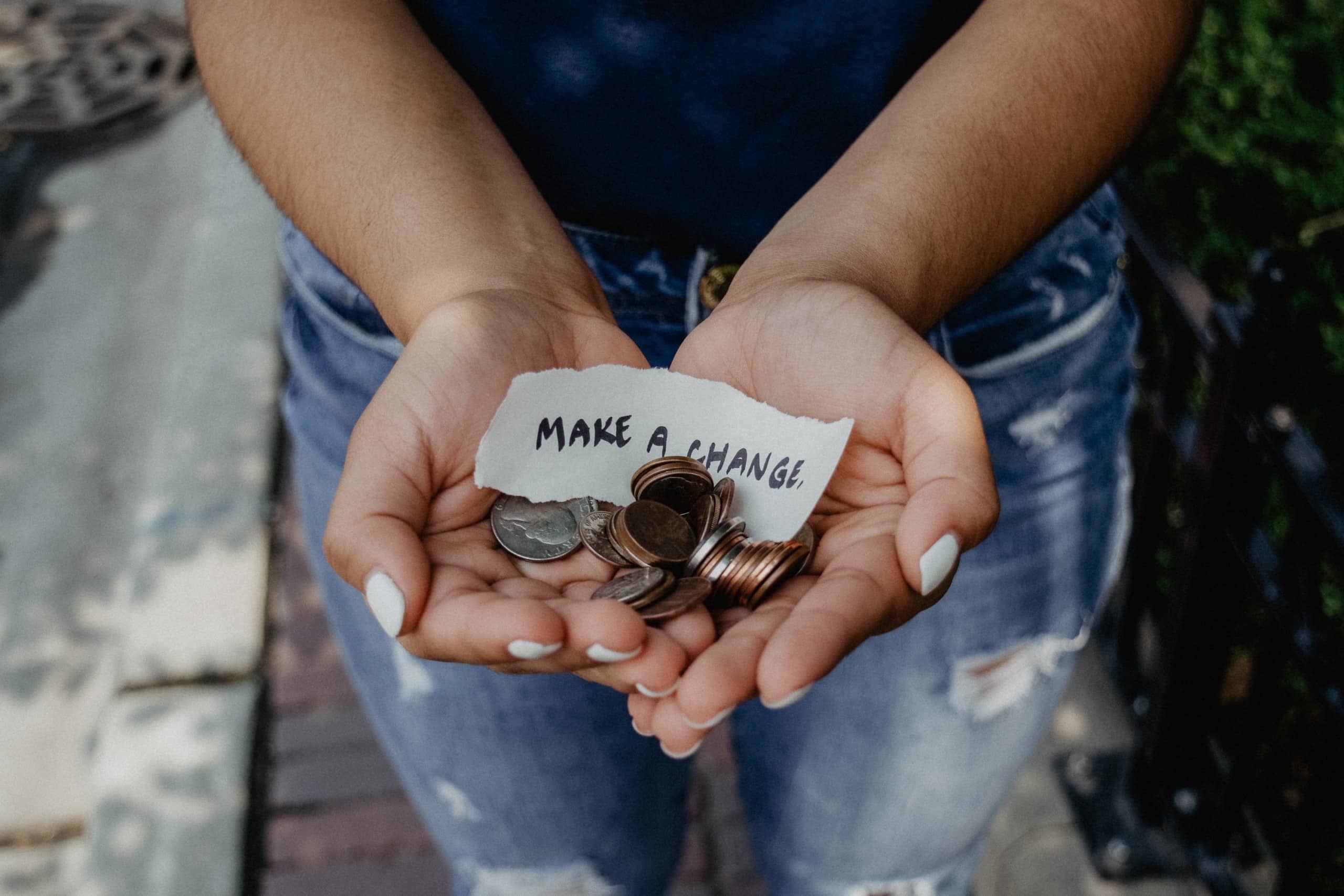 Mãos em concha segurando moedas e um papel escrito “make a change”.