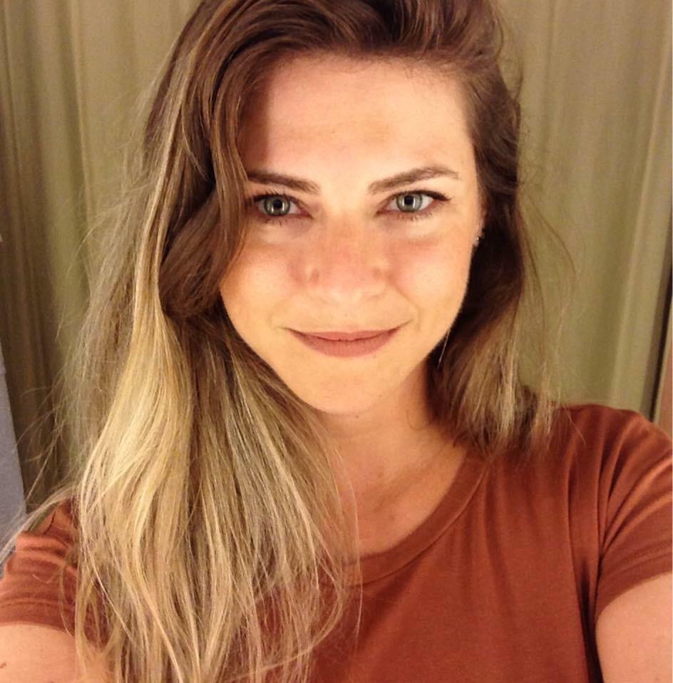 Retrato de uma mulher de cabelos longos e camiseta cor de tijolo, sorrindo levemente.